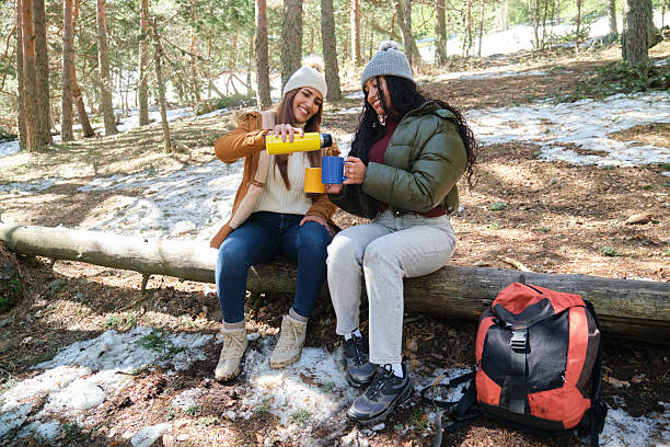 Close-up hiker's hands holding thermos and pouring a hot drink into a handcrafted wooden cup. Captured outdoors, the scene conveys warmth and relaxation amidst a natural setting. A refreshing escape in a serene atmosphere.