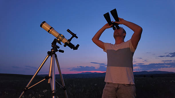 Amateur astronomer using telescope and binoculars for watching stars, Moon, planets and other celestial objects from a countryside field in nature.