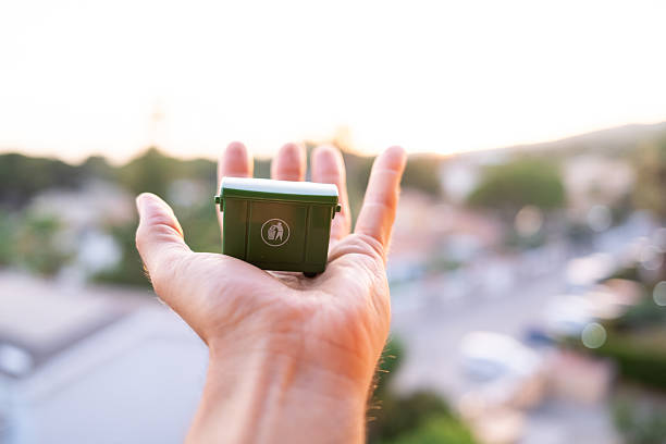 Hand holds a miniature garbage bin against a blurred city backdrop, symbolizing individual responsibility in waste management and environmental protection