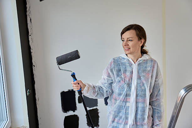 istock Woman in protective suit painting wall with black paint using roller during home renovation 2220392594