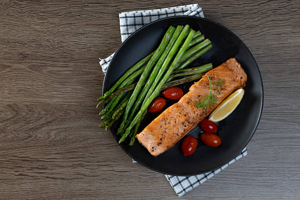 istock Grilled Salmon with Asparagus, Tomatoes and Lemon on Black Plate 2220394187