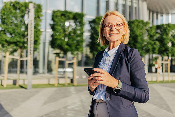 istock Confident woman smiling while using smartphone outdoors 2220396378