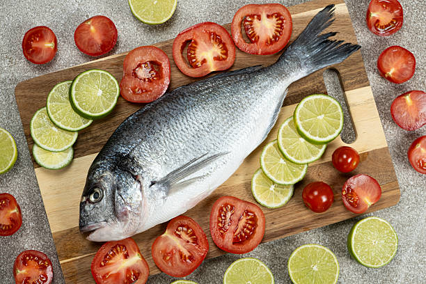 istock Raw Sea Bream with Lime and Tomatoes on Kitchen Counter 2220400446