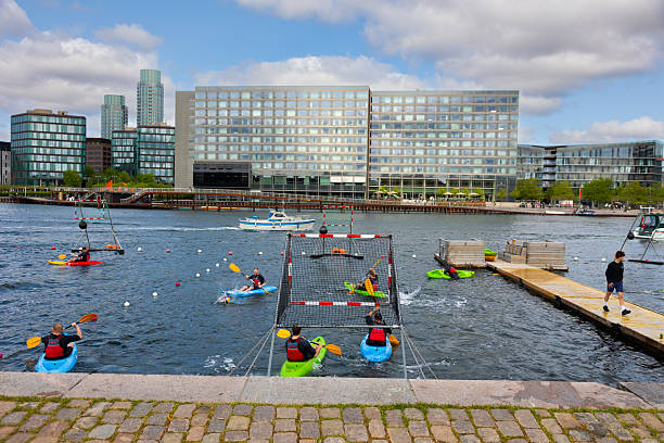 On a sunny summer morning a group of young men is playing canoe polo at Havneparken Islands Brygge Park of Copenhagen.