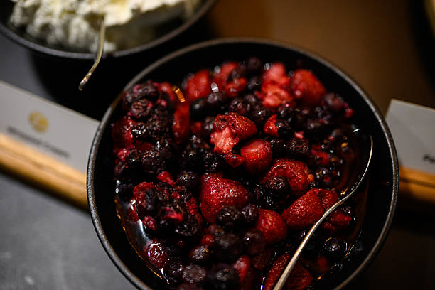 High angle view of a dark bowl brimming with a mixture of fresh red and dark berries with a juicy texture.