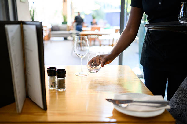 istock Female server setting wooden restaurant table with wine glasses at a hotel 2220402627