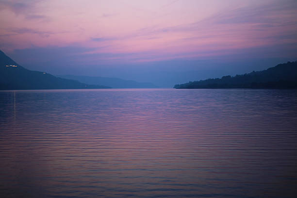 Evening scene at Mulshi Lake in Maharashtra, India, showing calm water, silhouetted trees, and hills under a purple and blue twilight sky.
