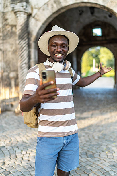 Young man vlogging in front of ancient arch, using smartphone and headphones