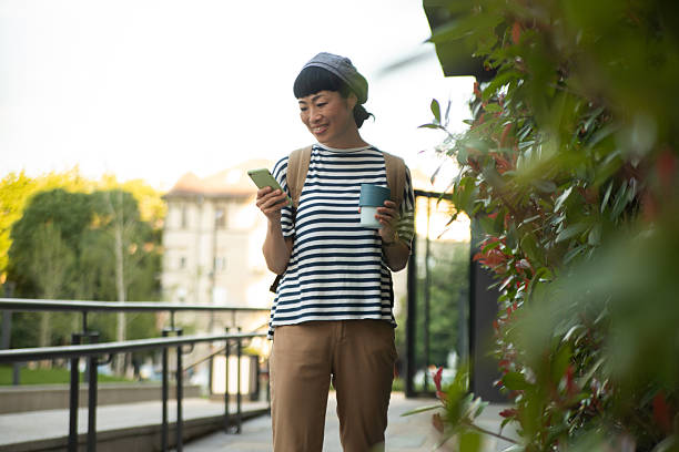 istock Young woman using smartphone and holding reusable coffee cup outdoors 2220403865