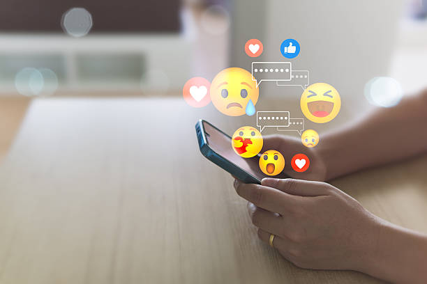 istock Social media concepts include exchange of ideas, socializing through the internet, technology, and social networking. A woman uses a mobile phone to send emojis to her friends while relaxing at home. 2220404365