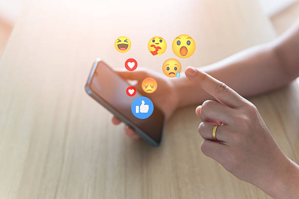 istock Social media concepts include exchange of ideas, socializing through the internet, technology, and social networking. A woman uses a mobile phone to send emojis to her friends while relaxing at home. 2220404366