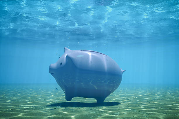 Piggy bank placed underwater on the ocean floor, visualizing economic pressure, debt, or sinking investments.