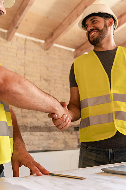 istock Male Construction worker and architect shaking hands over blueprint in building under construction 2220406753