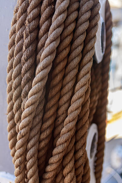 istock Closeup of twisted brown ship ropes wrapped around metal pulley element. 2220407162