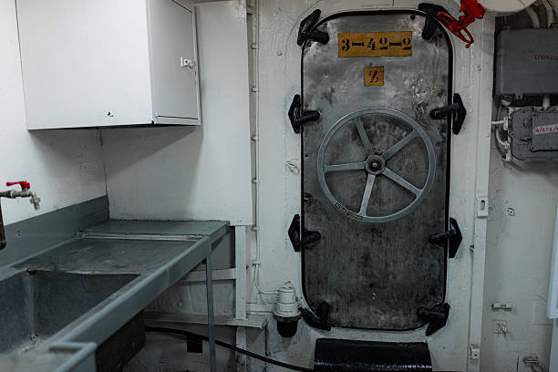 istock Industrial ship interior with metal door and heavy wheel handle under low light. 2220407220