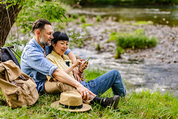 istock Couple enjoying a sunny day by the riverbank while using a smartphone in a serene natural environment 2220407816
