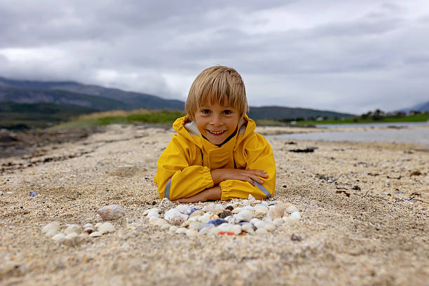 Beautiful blond child, boy, gathering shells on a beach in Norway, making heart from them