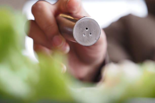 A hand is poised to sprinkle salt over a vibrant salad during lunch.