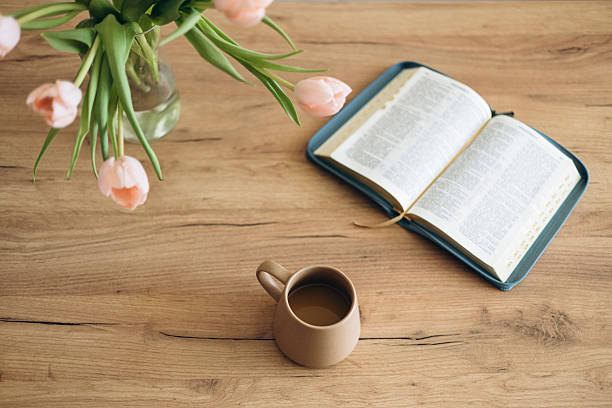 istock Open Bible on a wooden table and ceramic coffee mug and a vase with tulips. 2220410093