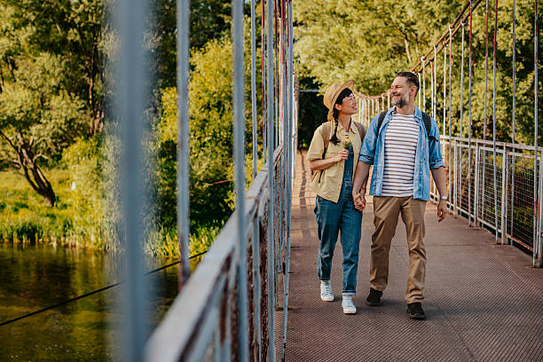 istock Couple enjoys a sunny day while walking hand in hand through nature on a bridge surrounded by greenery 2220412155