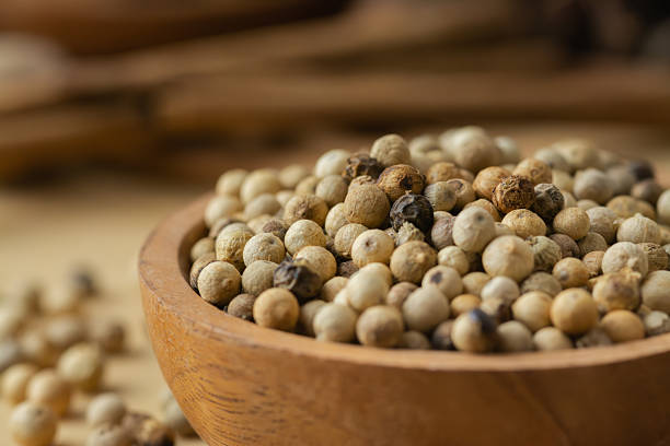 A detailed close-up of dried pepper grains captured indoors with artistic composition and warm lighting. The textured surface and natural tones enhance the organic feel of this spice, making it ideal for culinary blogs, food packaging, kitchen visuals, or herbal product content. Perfect for showcasing spice detail in a refined and rustic setting.