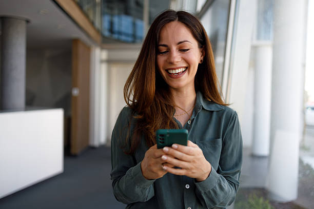 istock Professional female professional checking smartphone, smiling while networking in sleek corporate lobby during workday 2220415752