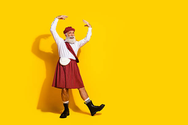 An elderly man wearing a traditional Scottish kilt and hat, performing a graceful dance with a joyful expression against a bright yellow background.