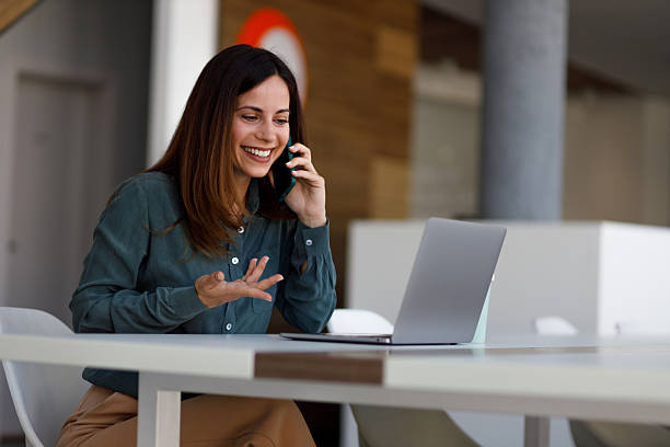 istock Professional businesswoman multitasking, talking on smartphone while typing on laptop at modern workspace 2220420916