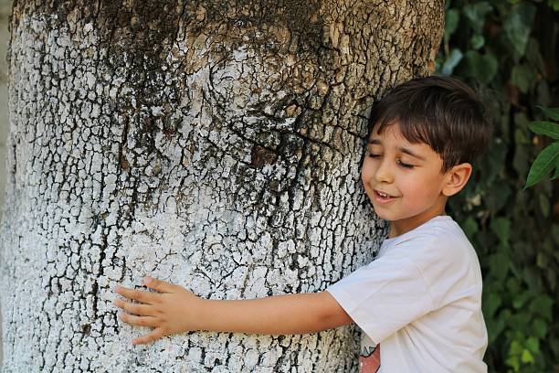 Smiling young boy sitting on a thick tree branch, looking at the camera.