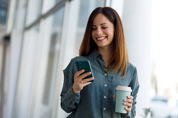 istock Professional woman working on smartphone, carrying eco-friendly coffee mug while navigating corporate corridor 2220422795