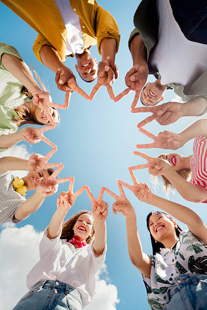 istock Group of diverse best friends enjoying fun outdoors under blue summer sky bonding and forming shapes with hands 2220424604