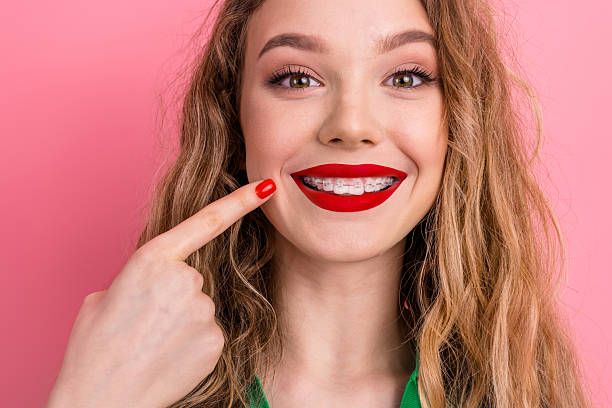 istock Stylish young woman with braces on pink background showing a joyful expression and sporting vibrant cosmetics. 2220425665