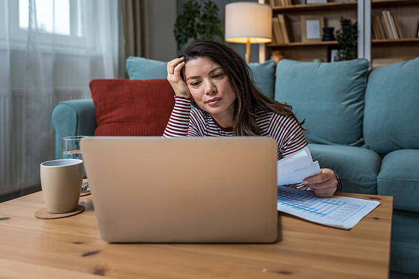 istock Young woman struggling with focus while working on laptop on floor, surrounded by printed analytic, battling ADHD, mental fatigue, burnout, and the pressure of modern multitasking expectations 2220428455