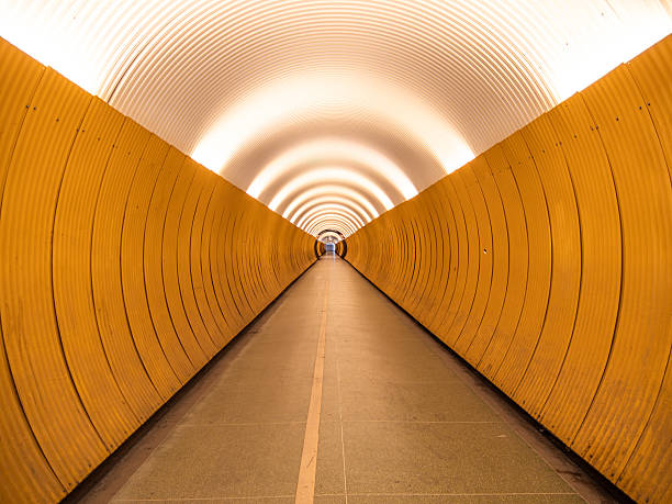 Stockholm, Sweden - May 11th 2025: A long, curving tunnel with smooth yellow walls and a bright, illuminated ceiling. The perspective creates a sense of depth, leading to a distant light at the end.