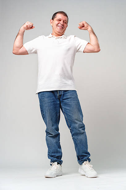 istock Happy older man showing off his strong biceps while standing against a light gray background 2220430037