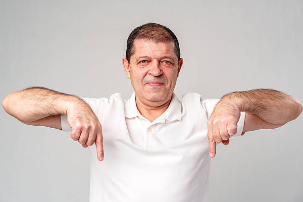 istock A man in a white shirt smiling and gesturing downwards in a studio with a light gray background 2220430371