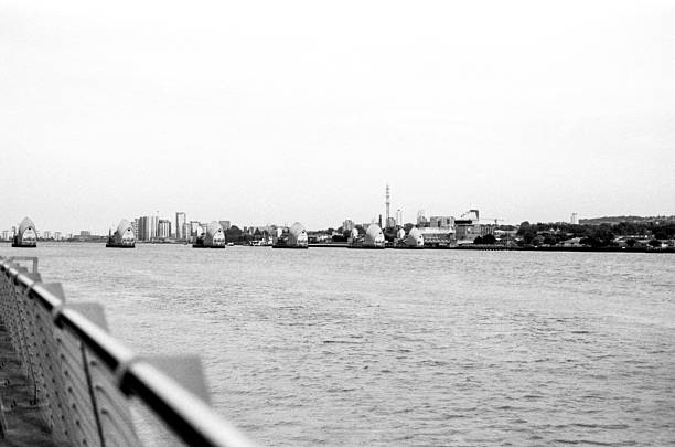 Grainy black and white analog photo capturing the thames barrier, a vital flood protection structure for london, viewed from the riverbank on a clear daytime