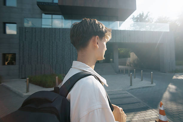 istock Schoolboy standing alone outside school building with backpack, back view 2220434410
