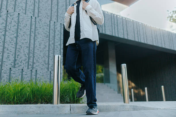 istock Confident young man walking outside modern office building with backpack 2220434432