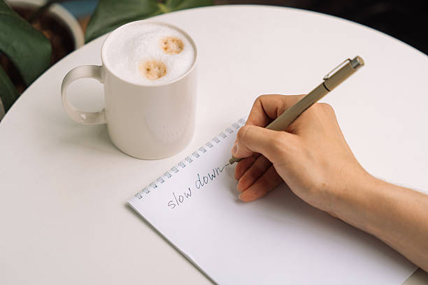 istock Handwriting slow down in notebook next to a mug of cappuccino on a round table. 2220440254