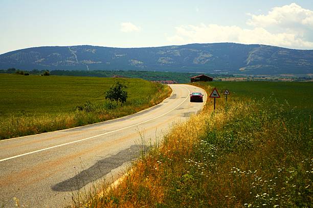 An asphalt road between meadows and mountains
