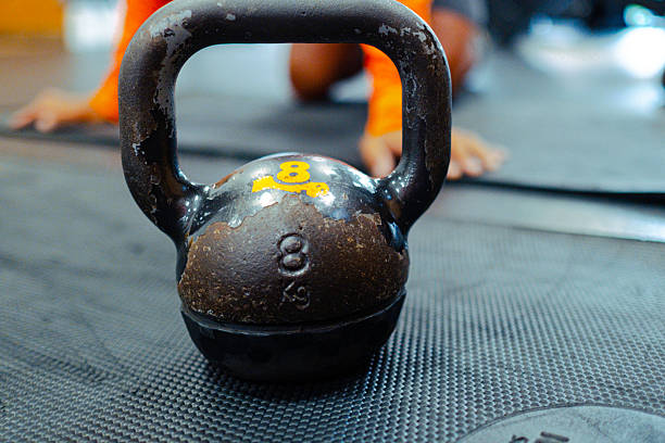 Close-up of an 8kg kettlebell on a gym floor, with an athlete stretching in the background, ready for a workout