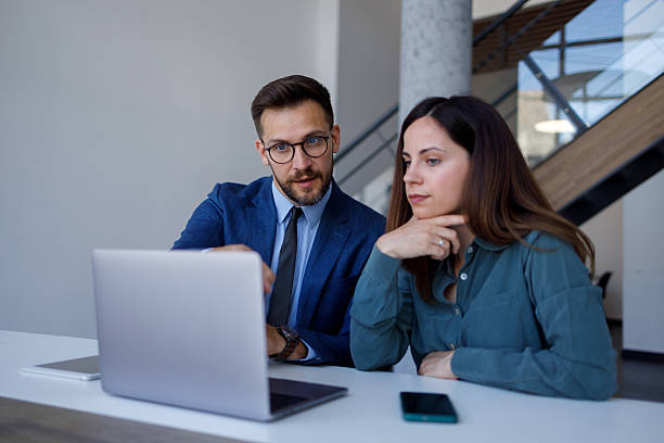 istock Two business professionals are working together, analyzing data and discussing strategies on a laptop in a bright, modern office 2220449710
