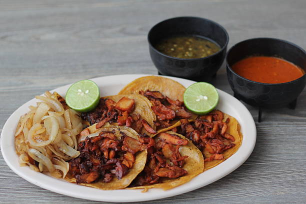 Sizzling al pastor tacos filled with succulent pork, garnished with fresh lime, accompanied by flavorful salsas and grilled onions, showcasing a delicious Mexican feast.