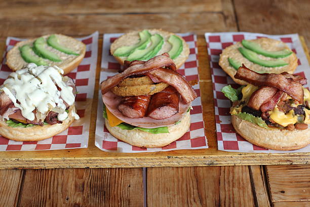 istock Three gourmet sandwiches stacked high with various toppings, including meats, cheeses, and veggies, presented on a rustic wooden board for a visually appealing meal. 2220452739