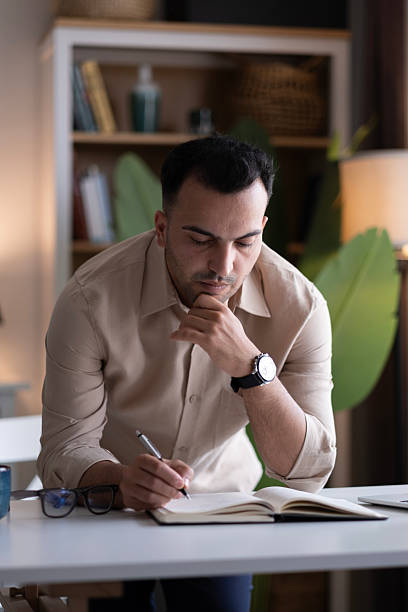 istock Young man writing in notebook at home 2220454138