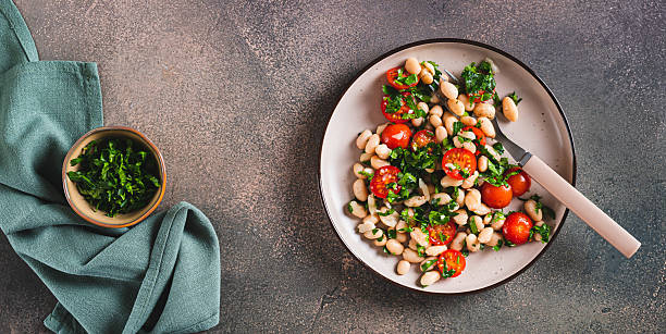 istock Vegetarian white bean, tomato and herb salad on a plate on the table top view web banner 2220454955