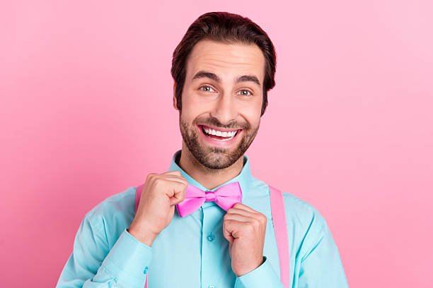 istock Photo of charming impressed young guy dressed teal clothes adjusting bowtie smiling isolated pink color background 2220456947