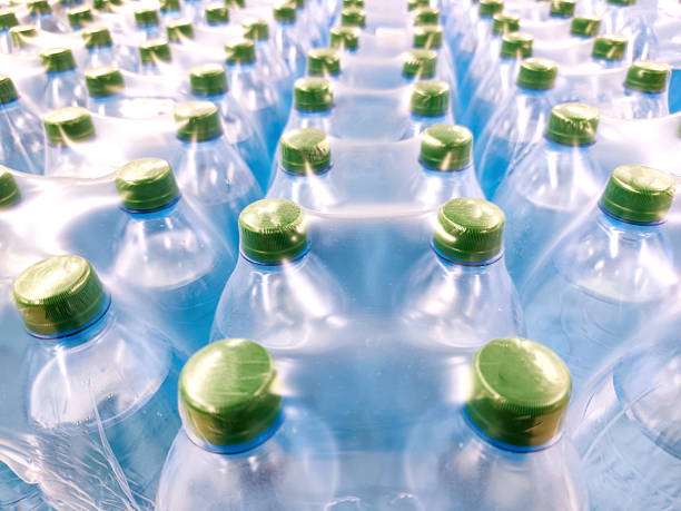 istock Multiple plastic water bottles tightly packed in shrink wrap, seen from above. Green caps, blue-toned bottles, clean, fresh visual, hydration, mass production, bottled water industry, packaging, and logistics. 2220463147