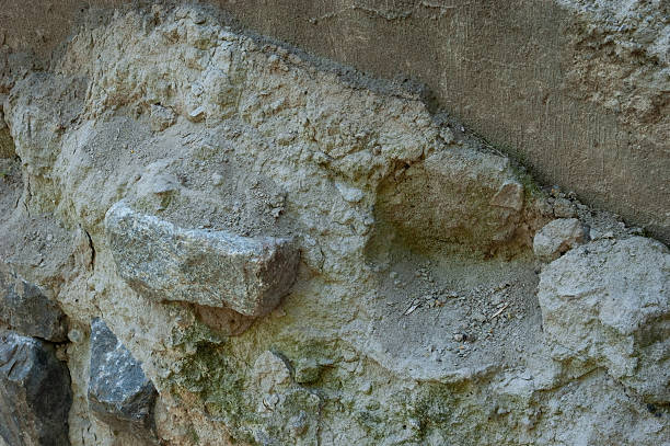 istock Concrete wall with granite pieces mostly crumbled. Cement between stones is cracked and worn, showing signs of age and decay. 2220463309